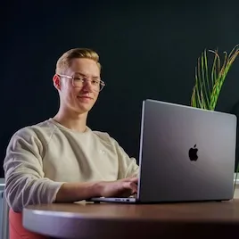 Piotr Pająk, programista, siedzący przy biurku z MacBookiem